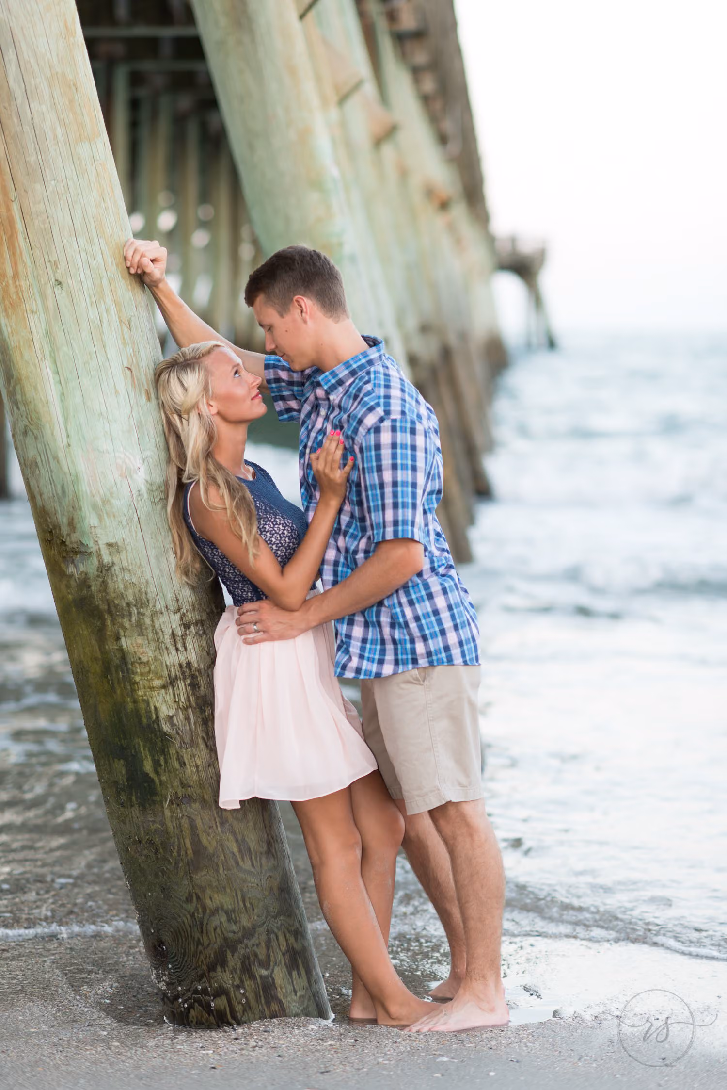 Woman leaning back on a pier piling as her fiancé leans in close by the waves at Myrtle Beach State Park