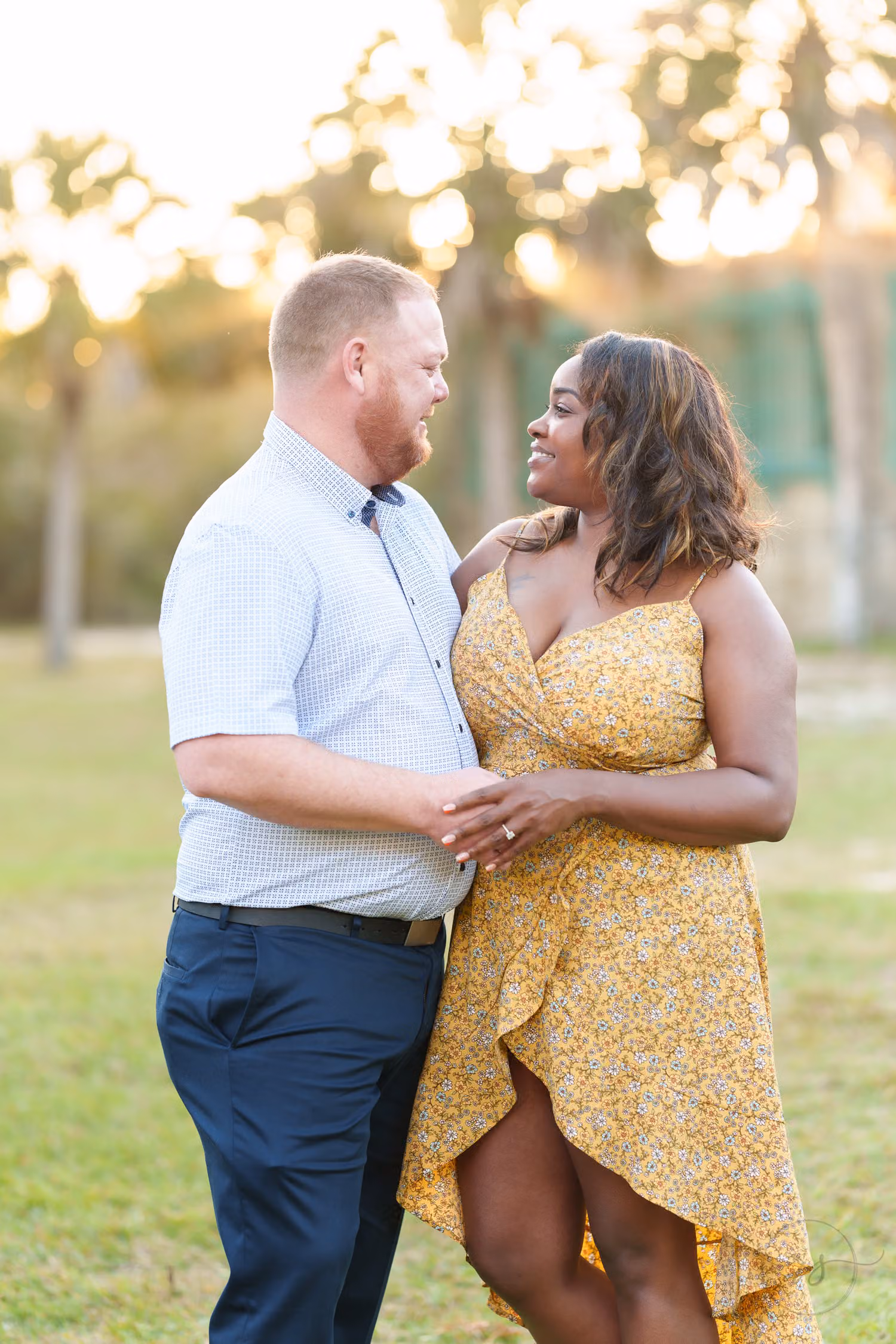 Couple smiling at each other in warm evening light on a grassy lawn under palm trees at Huntington Beach State Park