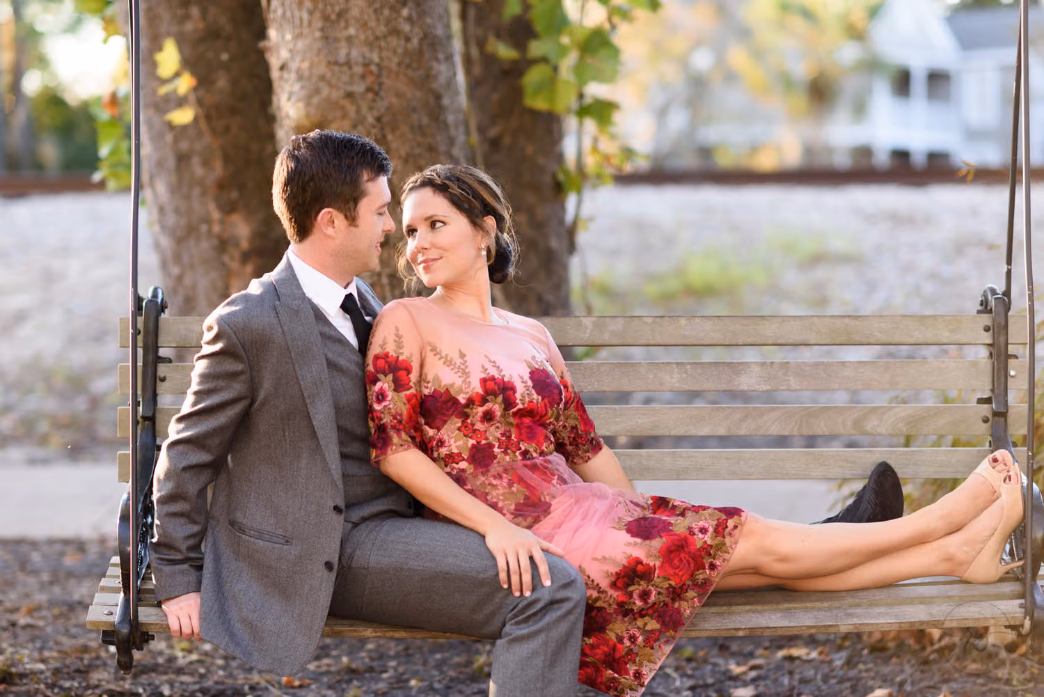 Couple lounging together on a wooden porch swing, she in a red floral dress, along the Conway Riverwalk