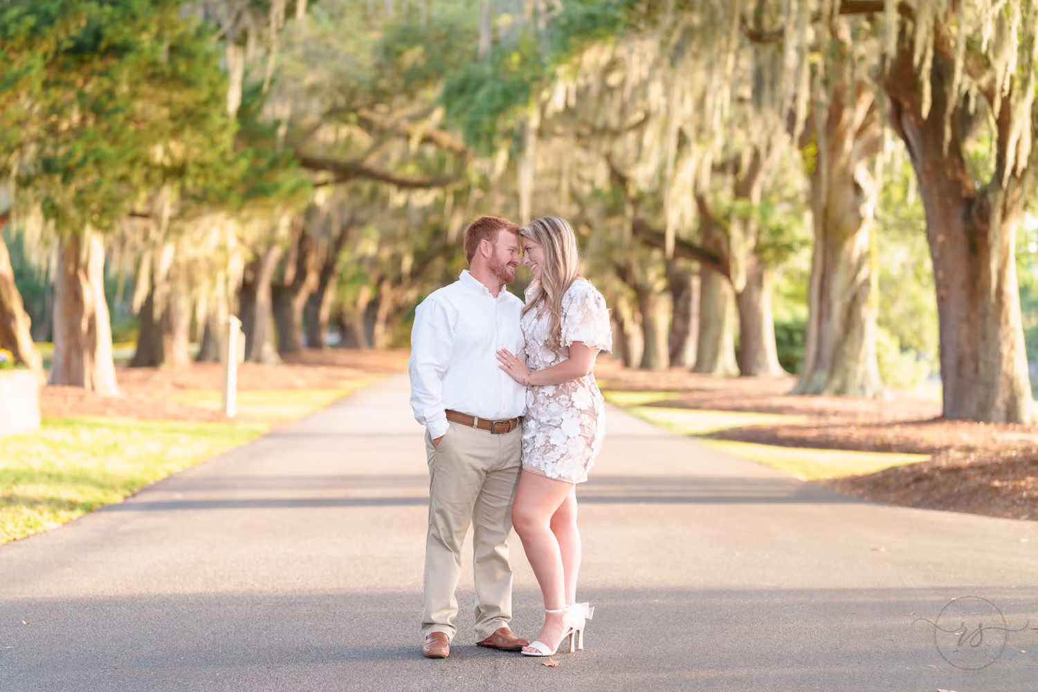 Couple standing close on the drive under a long row of oaks draped in Spanish moss at Caledonia Golf & Fish Club