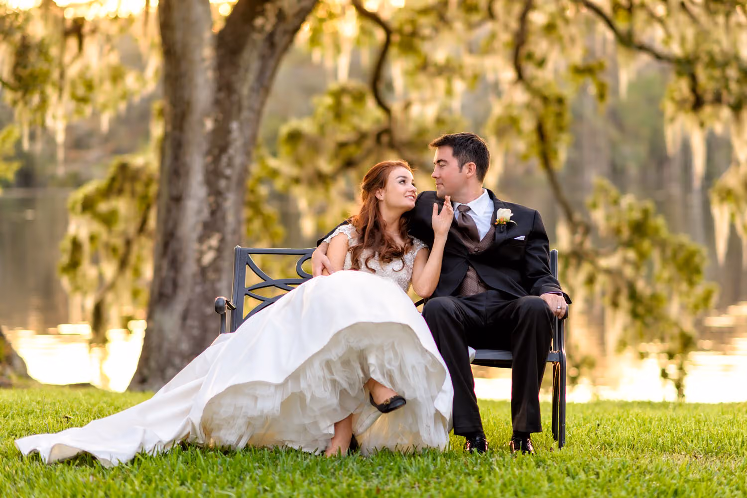 Bride and groom sitting close on a bench under a mossy oak at sunset by the Waccamaw River at Wachesaw Plantation