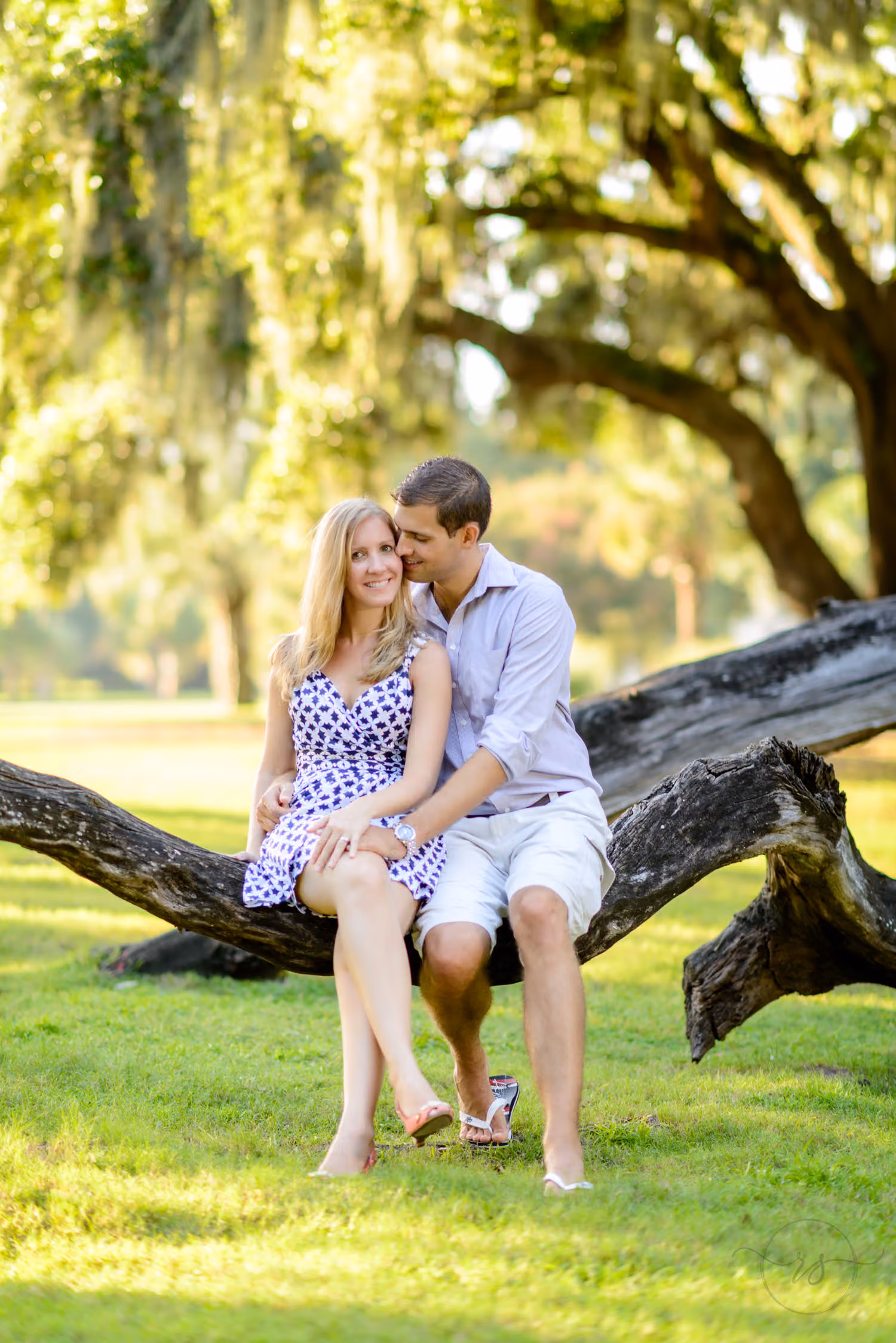 Couple sitting side by side on a fallen oak branch on a green lawn under mossy trees in Litchfield