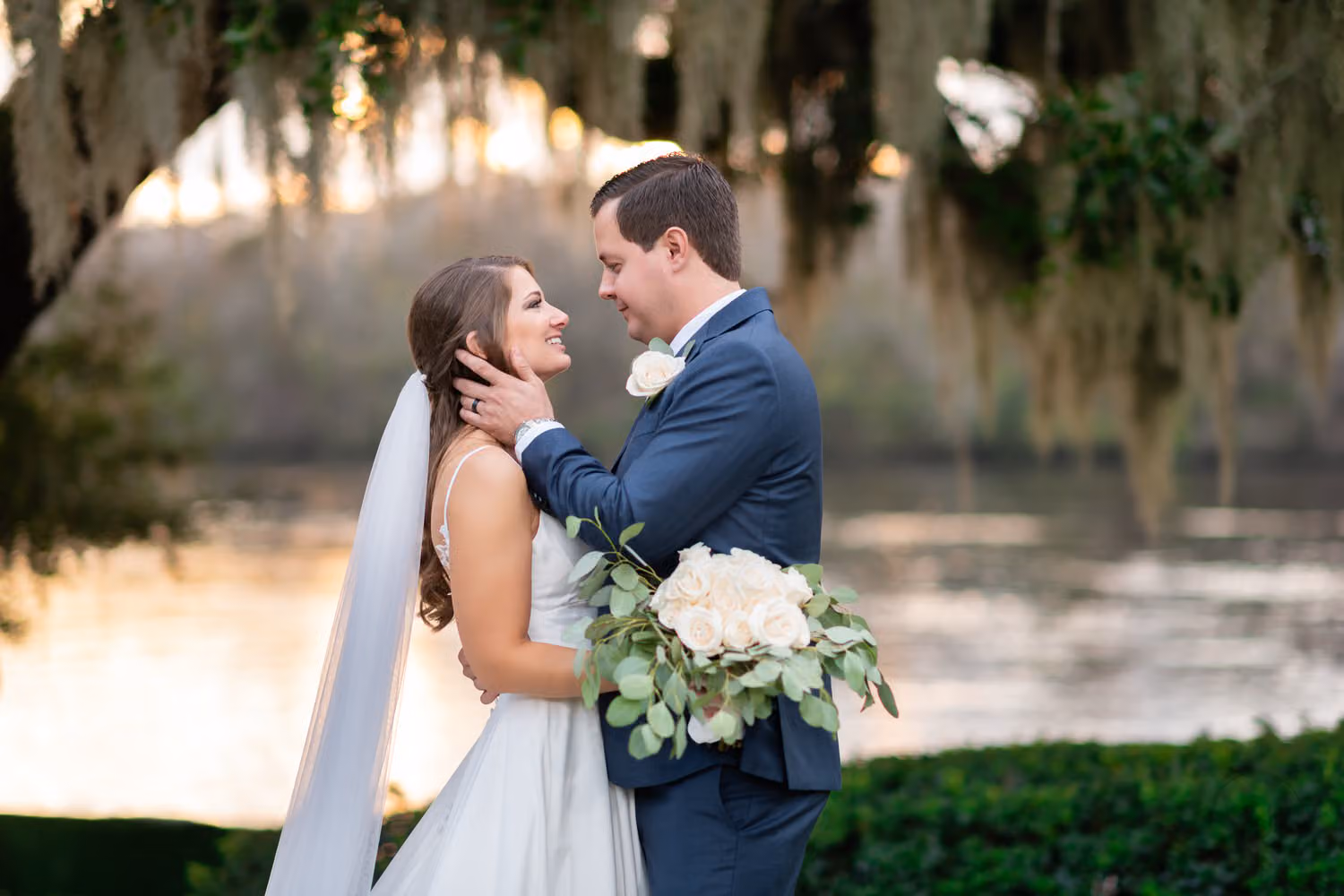 Bride and groom smiling at each other under Spanish moss by the river at sunset at Kimbel's at Wachesaw Plantation