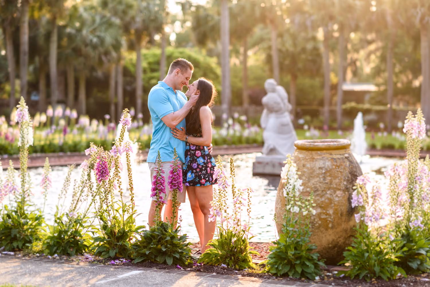 Couple smiling at each other by a fountain surrounded by pink foxgloves and palm trees at Brookgreen Gardens