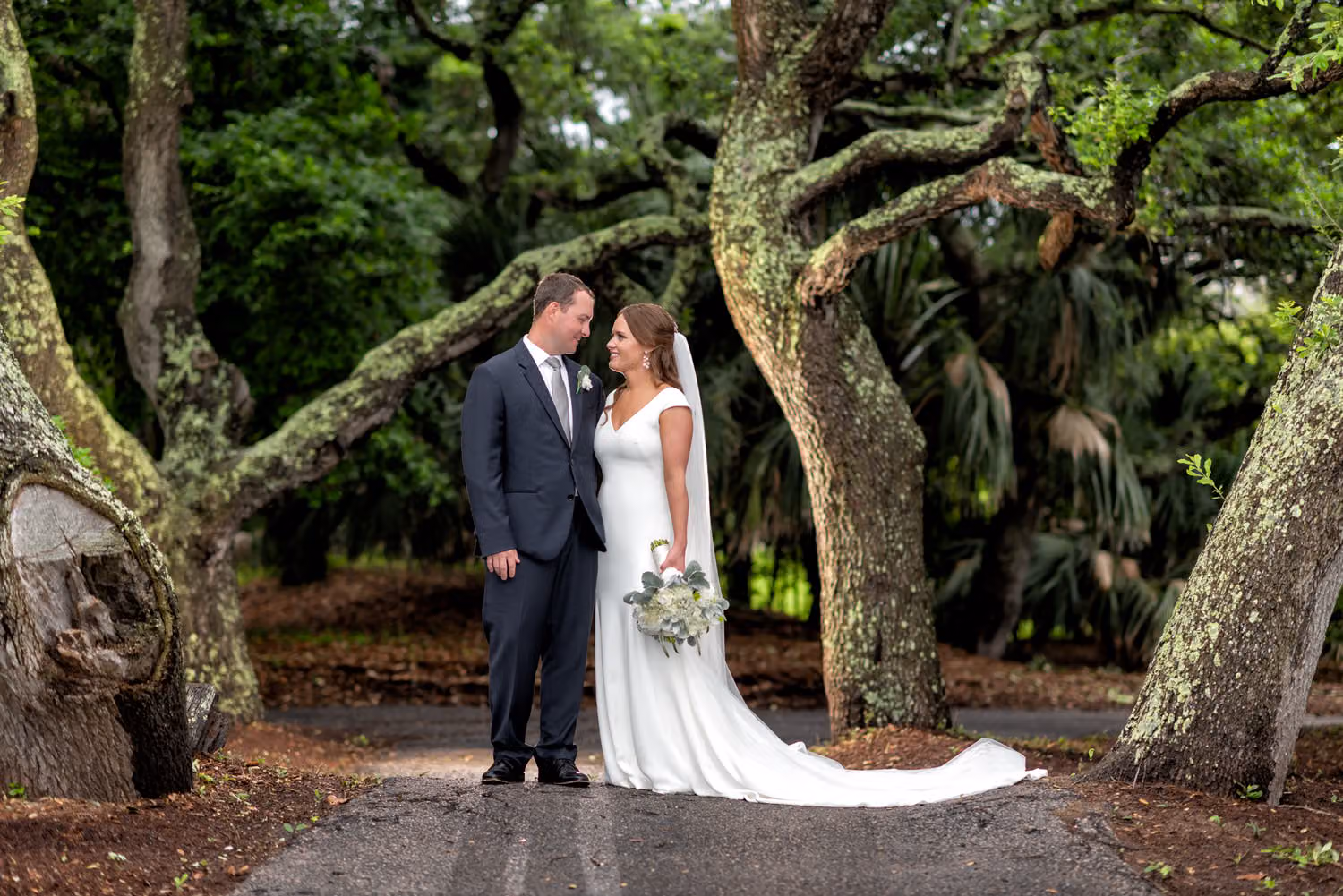 Bride and groom standing together on a path framed by twisting old oak trunks at Dunes Golf and Beach Club