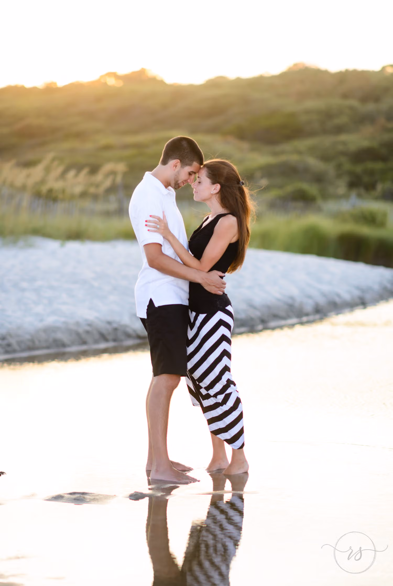 Couple about to kiss at the edge of a tidal pool, their reflections on the wet sand at sunset at Myrtle Beach State Park