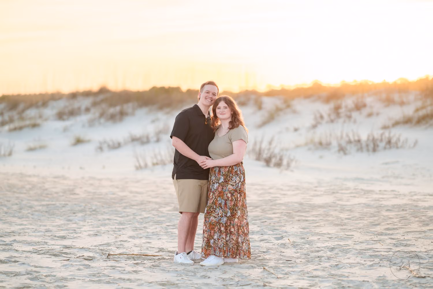 Couple hugging on the sand with the sunset glowing over the dunes and sea oats at Huntington Beach State Park