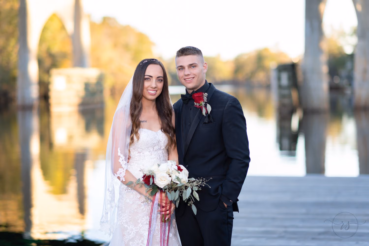 Bride holding her bouquet beside the groom on the dock with the Waccamaw River behind them at the Conway Riverwalk