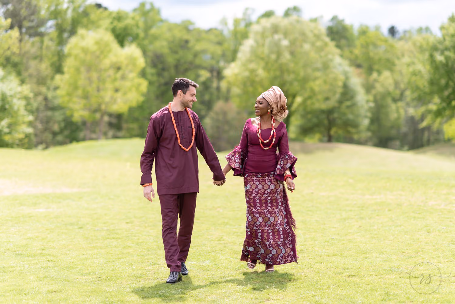 Bride and groom in traditional African wedding attire holding hands walking across the golf course at River Ridge Golf Club
