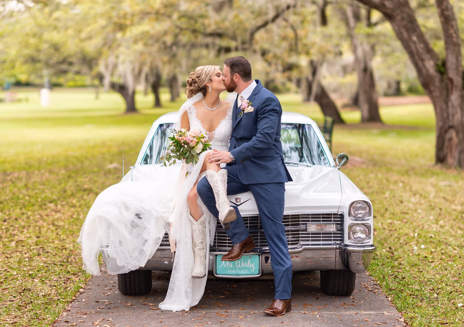 Bride and groom kissing while sitting on the front of a white classic car under the oaks at Brookgreen Gardens