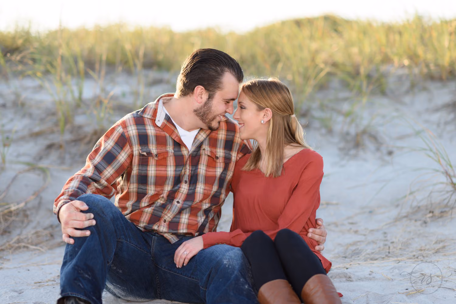 Couple sitting in the sand with their foreheads touching in front of the dunes at Myrtle Beach State Park