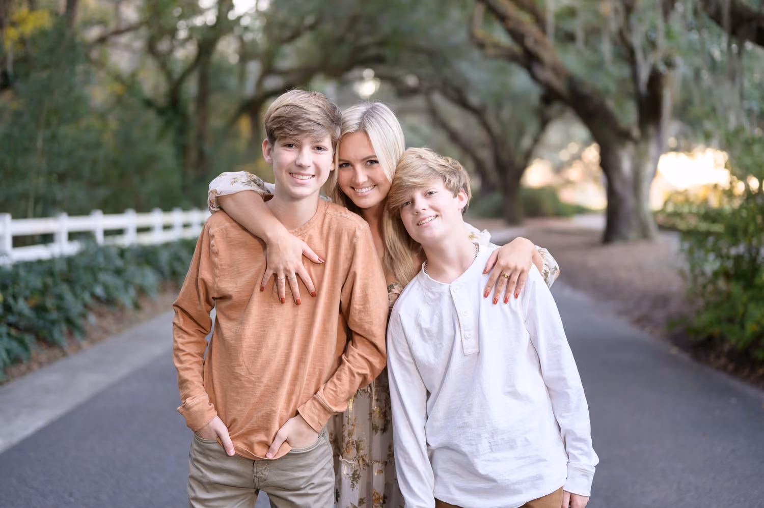 Sister wrapping her arms around her two brothers on the oak-lined avenue at Caledonia Golf & Fish Club