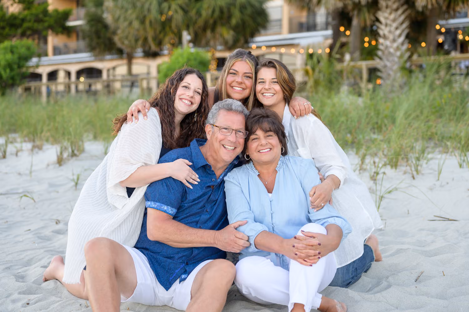 Grandparents sitting in the sand by the dunes with their grown daughters hugging behind them at Island Vista Resort
