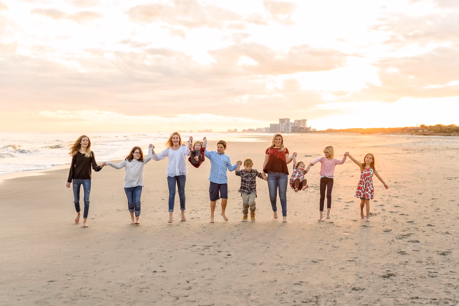 Group of kids holding hands and walking toward the camera on the beach at sunset at North Beach Plantation