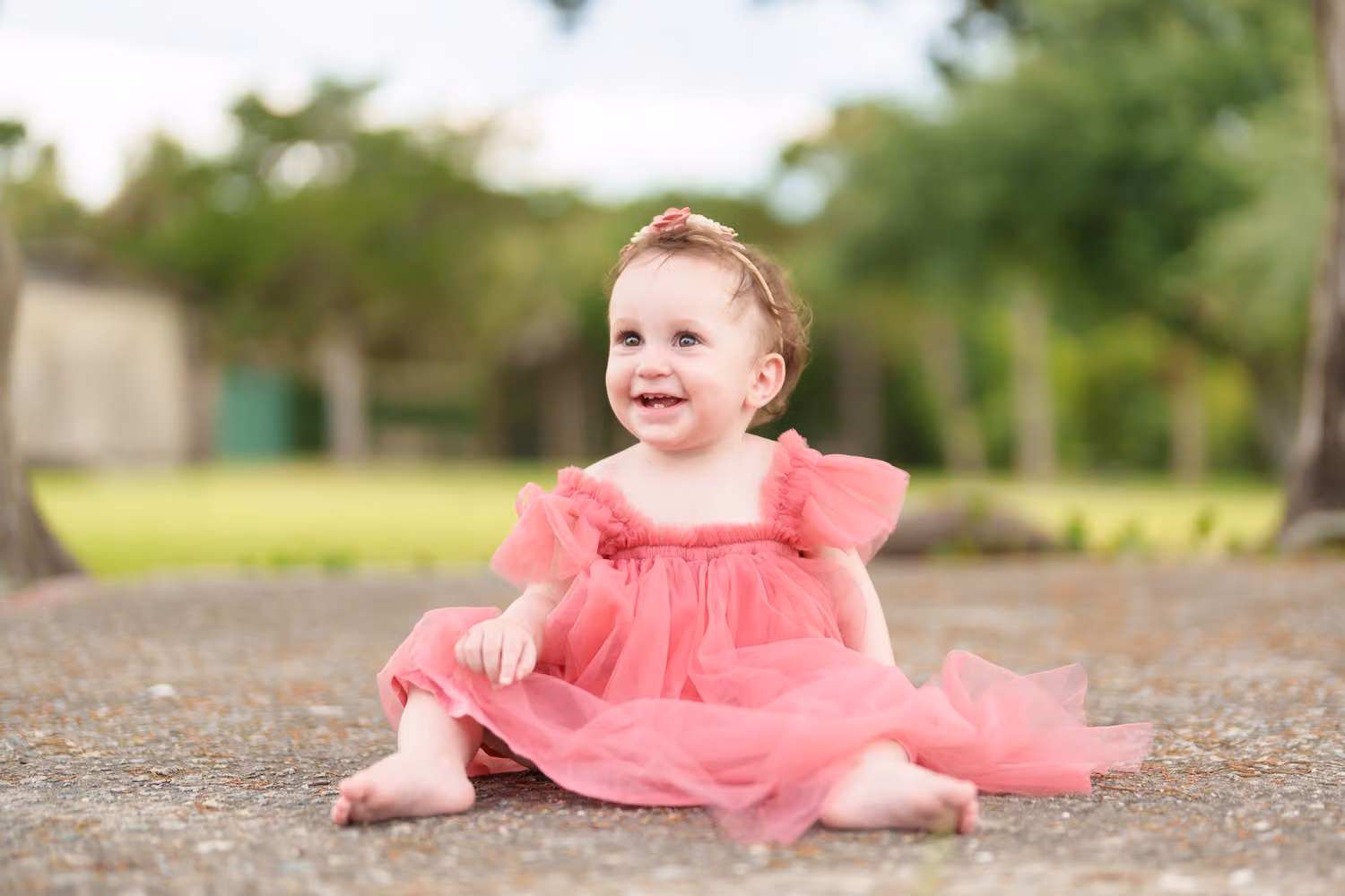 Baby girl in a coral tutu dress sitting and smiling on the path near Atalaya Castle at Huntington Beach State Park