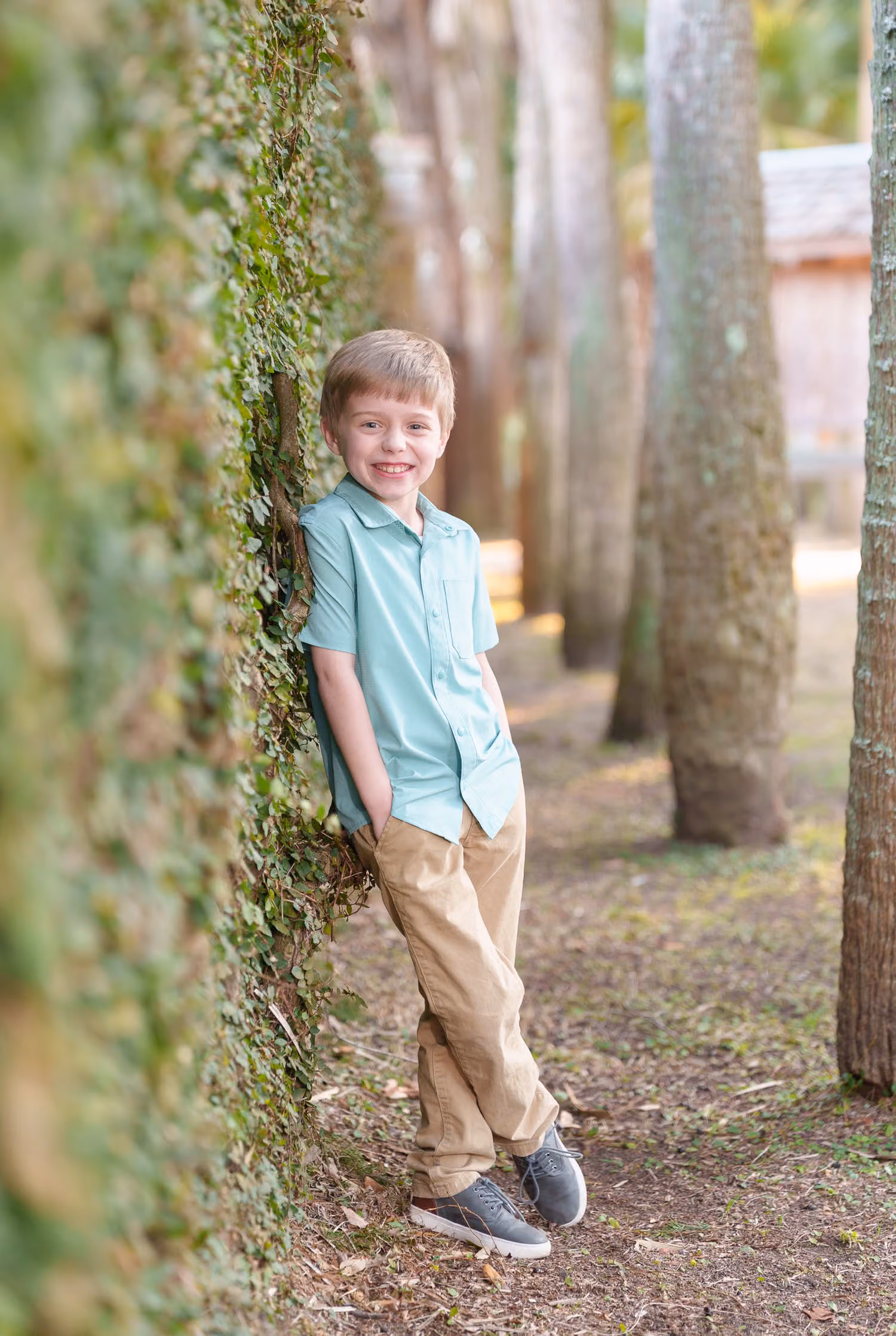 Boy in a teal shirt leaning against the ivy wall beside a row of palm trunks at Atalaya Castle, Huntington Beach State Park