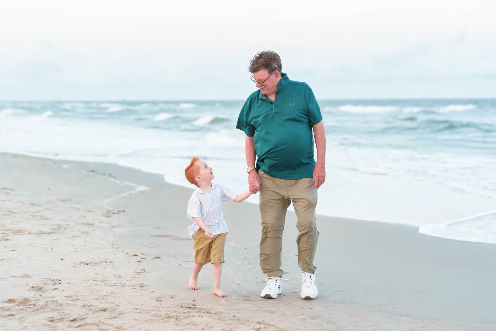 Little boy talking to his granddad holding hands walking down the beach - Huntington Beach State Park