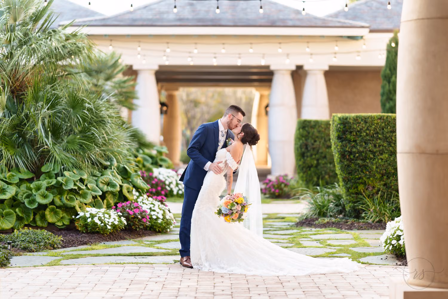 Groom in a navy suit dipping the bride for a kiss on the stone path of the courtyard at 21 Main Events