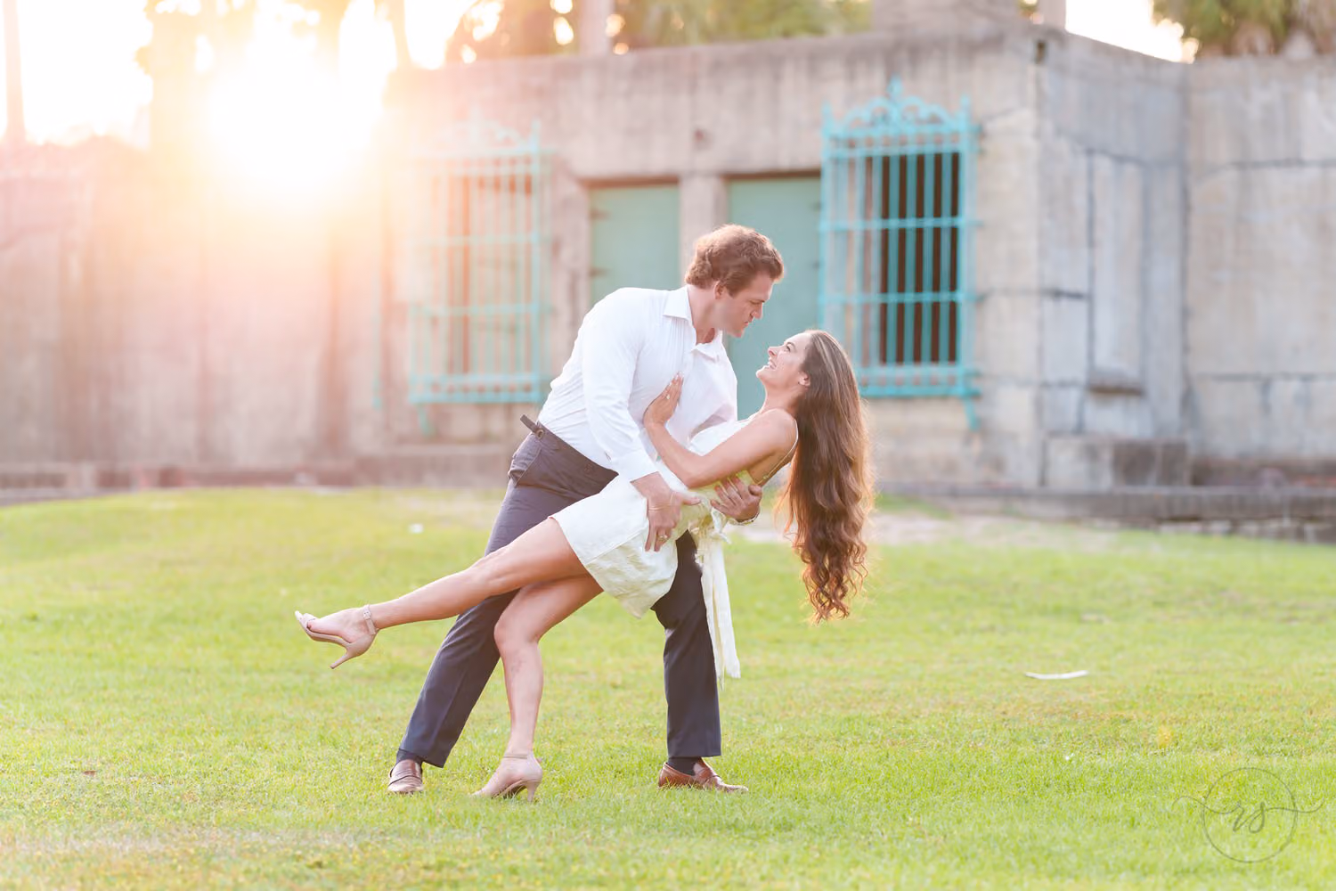 Man dipping his fiancée on the lawn as the sun shines over the Atalaya Castle wall at Huntington Beach State Park