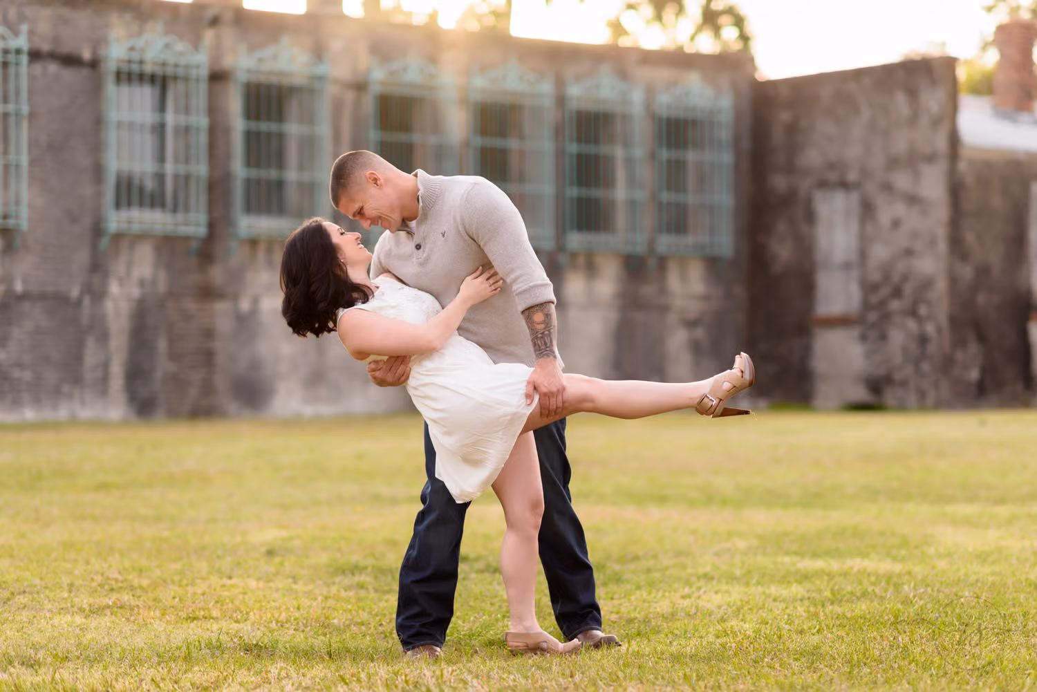 Man dipping his fiancée in a white dress on the lawn in front of the Atalaya Castle at Huntington Beach State Park