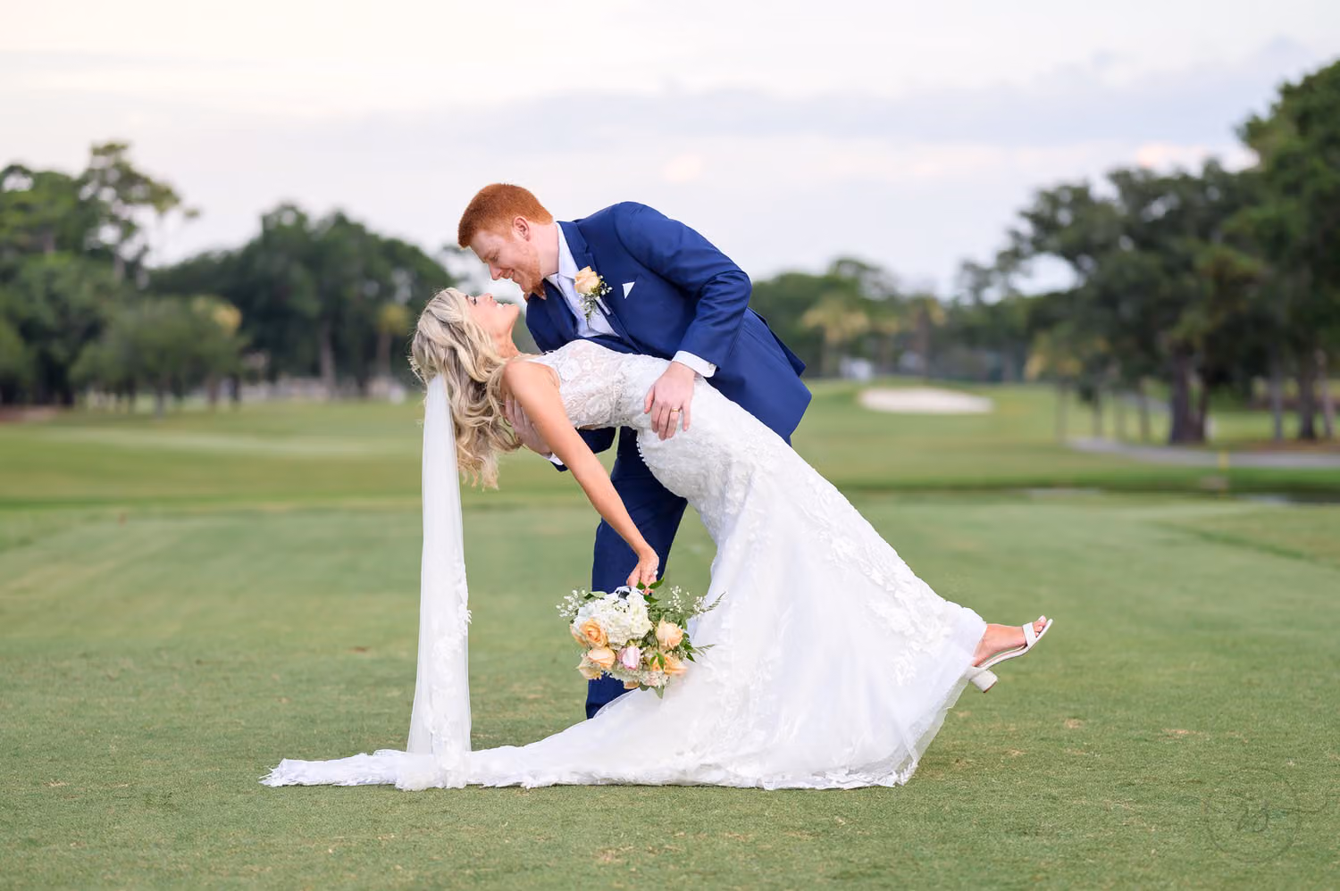 Groom in a navy suit dipping the bride for a kiss on the fairway at Dunes Golf & Beach Club