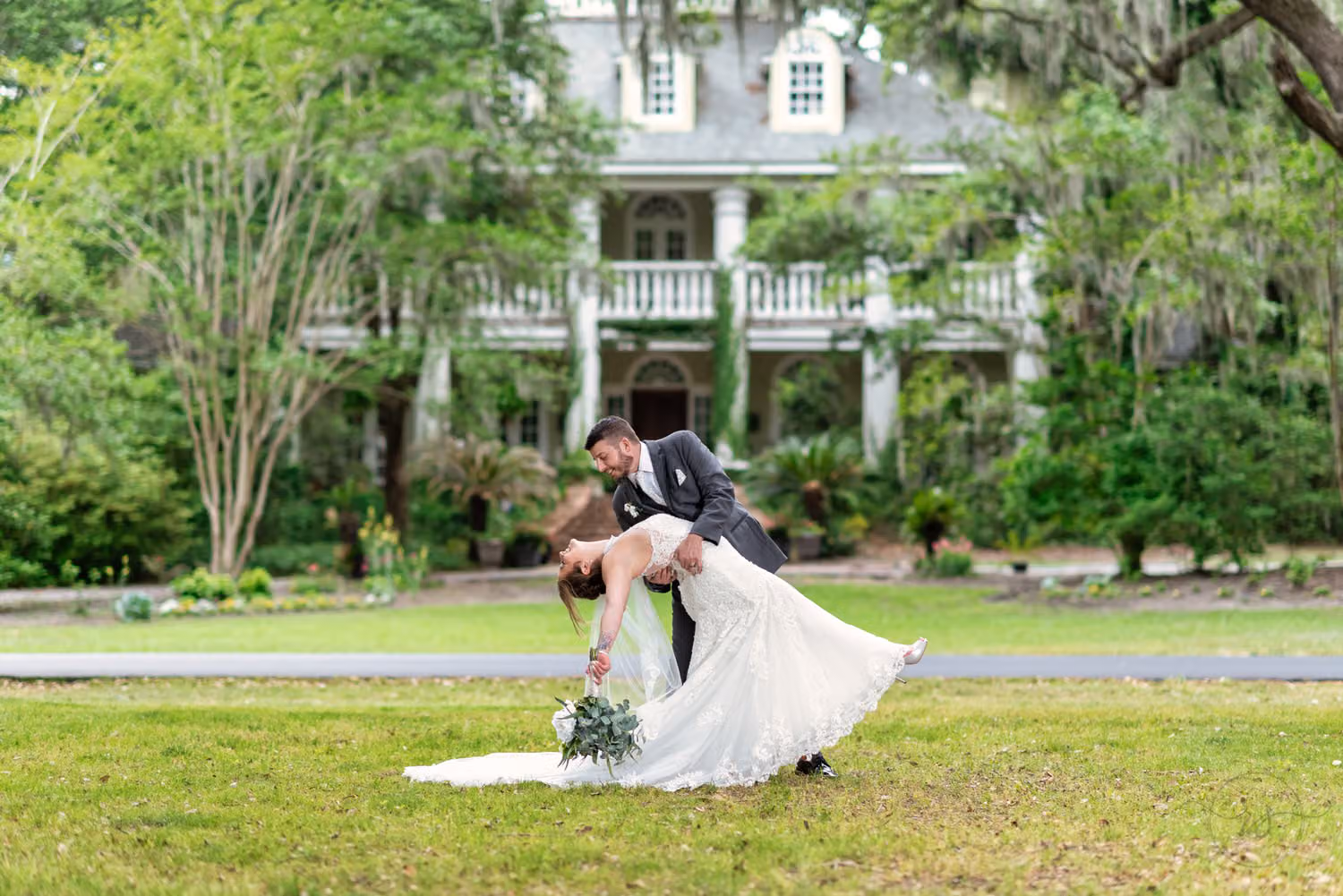 Groom dipping the bride on the lawn in front of the historic white plantation house at Wachesaw Plantation