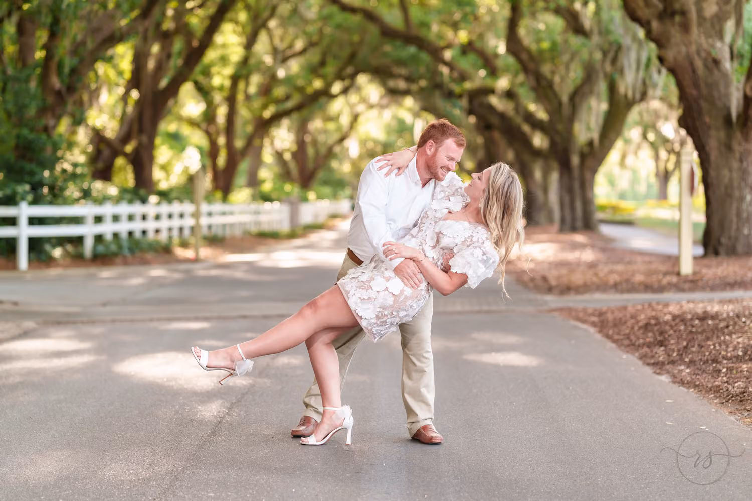 Man dipping his fiancée as she kicks up a heel on a road under the mossy live oaks at Caledonia Golf & Fish Club