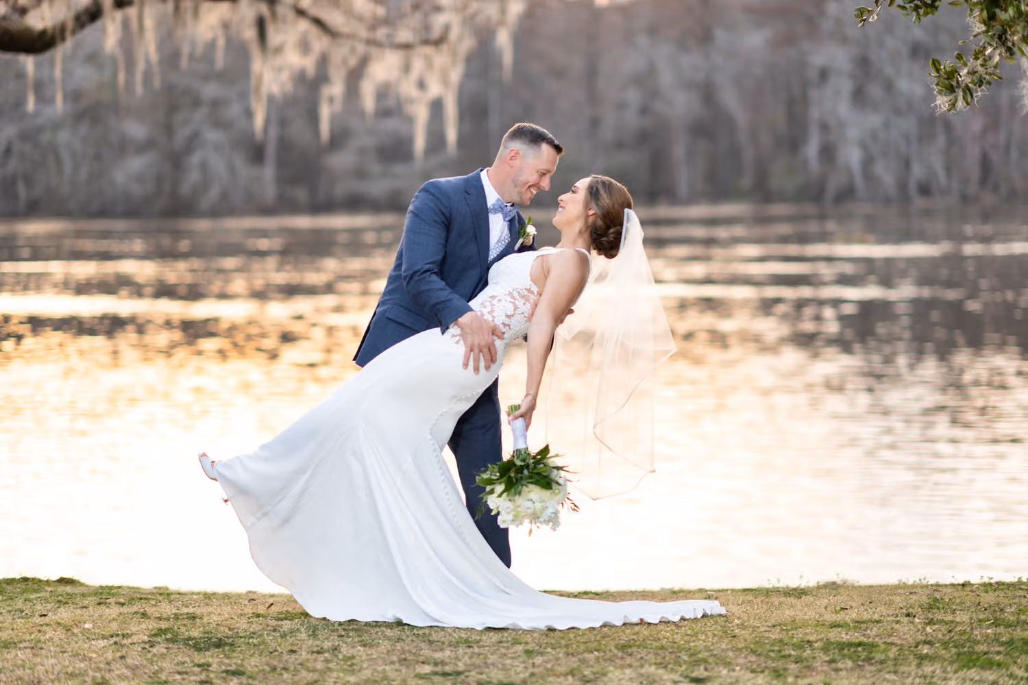 Groom dipping the bride with her veil flowing beside the Waccamaw River at sunset at Kimbel's at Wachesaw Plantation