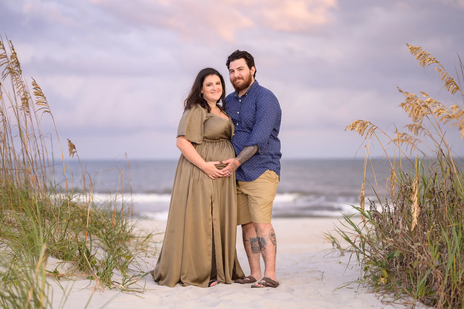 Expectant couple standing between clumps of sea oats on the beach under a purple evening sky at Huntington Beach State Park
