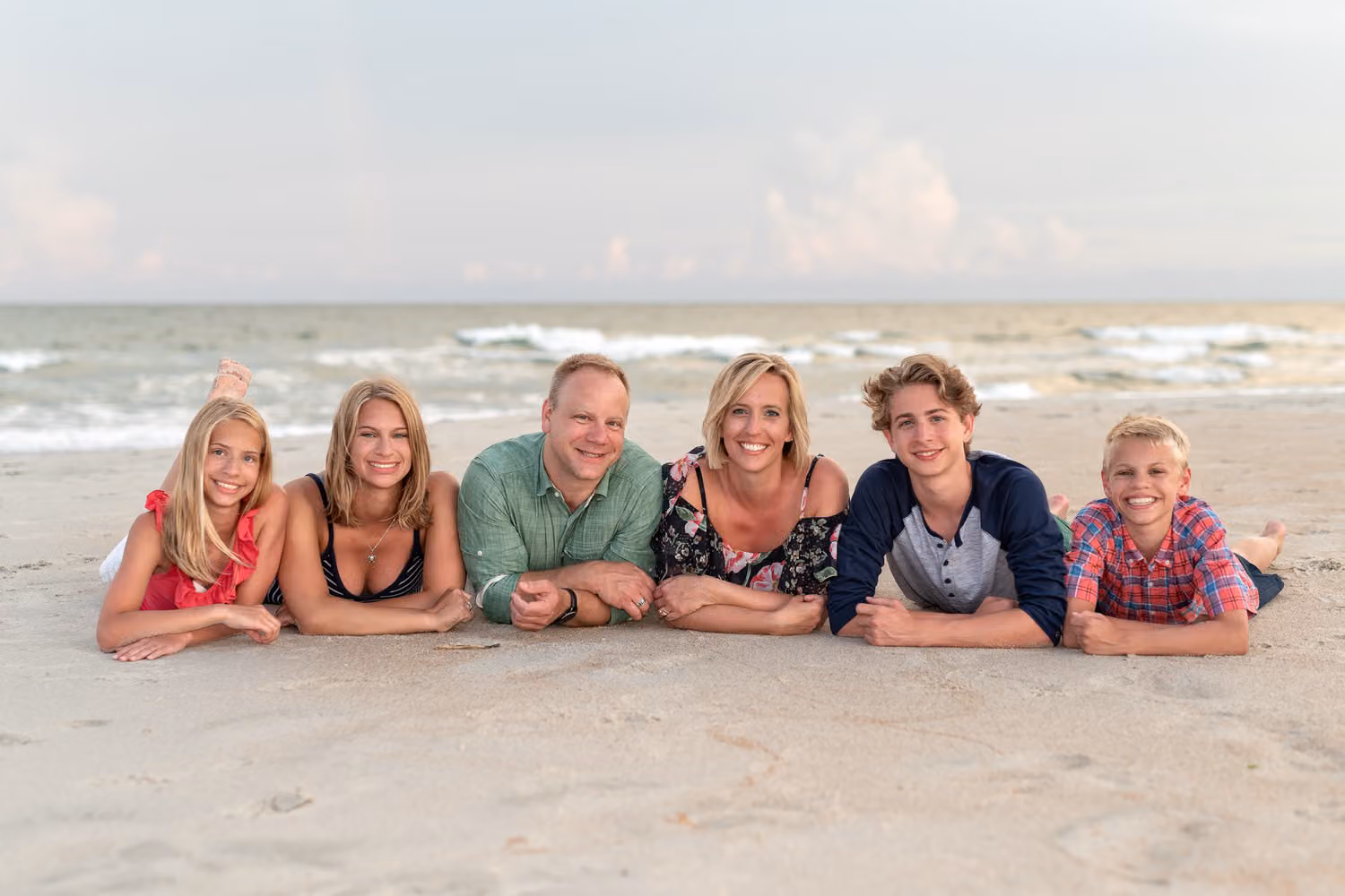 Family of six lying in a row on their stomachs in the sand by the ocean at Huntington Beach State Park