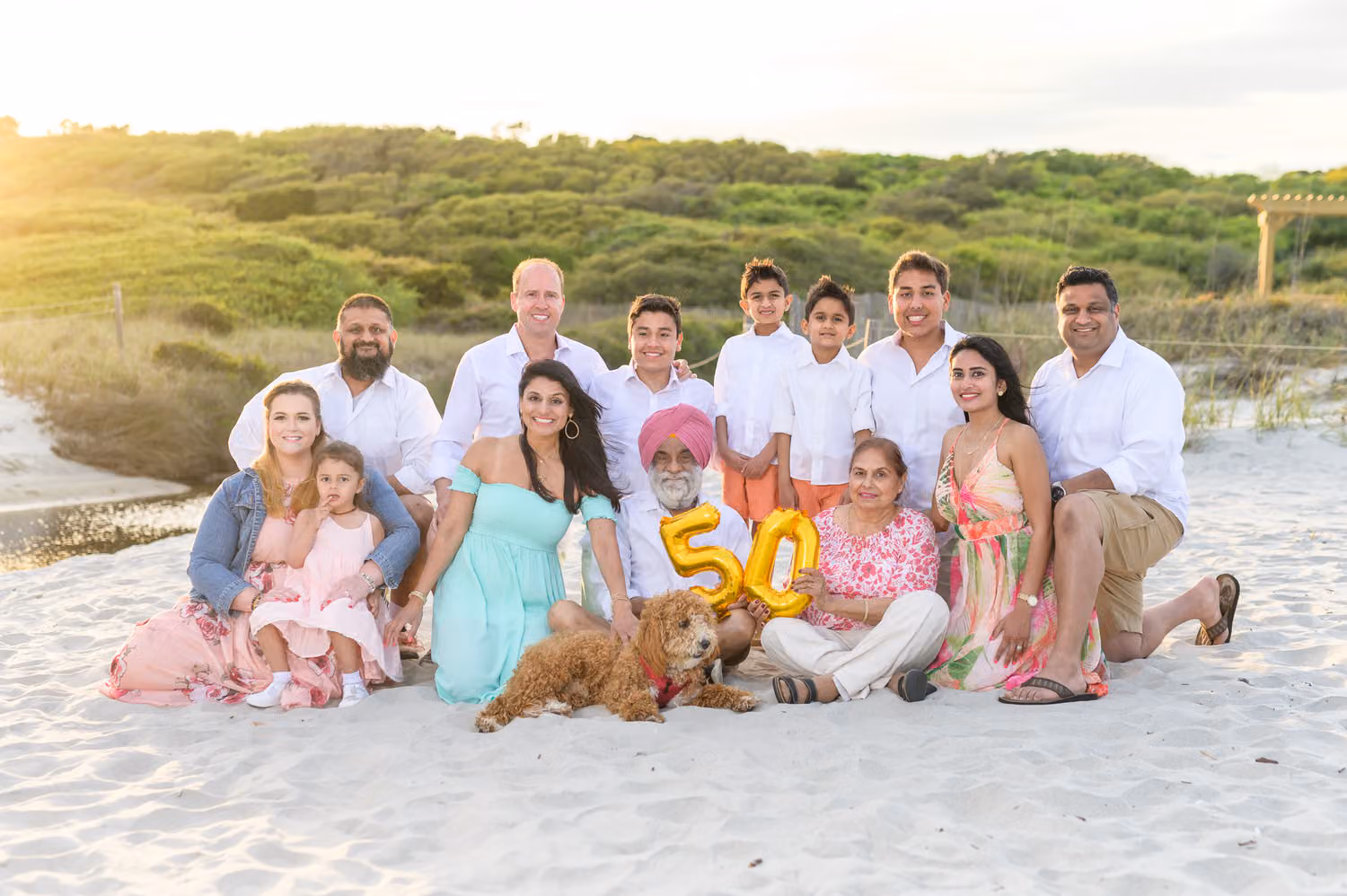 Extended family gathered in the sand with gold 50 balloons and their Goldendoodle at Myrtle Beach State Park