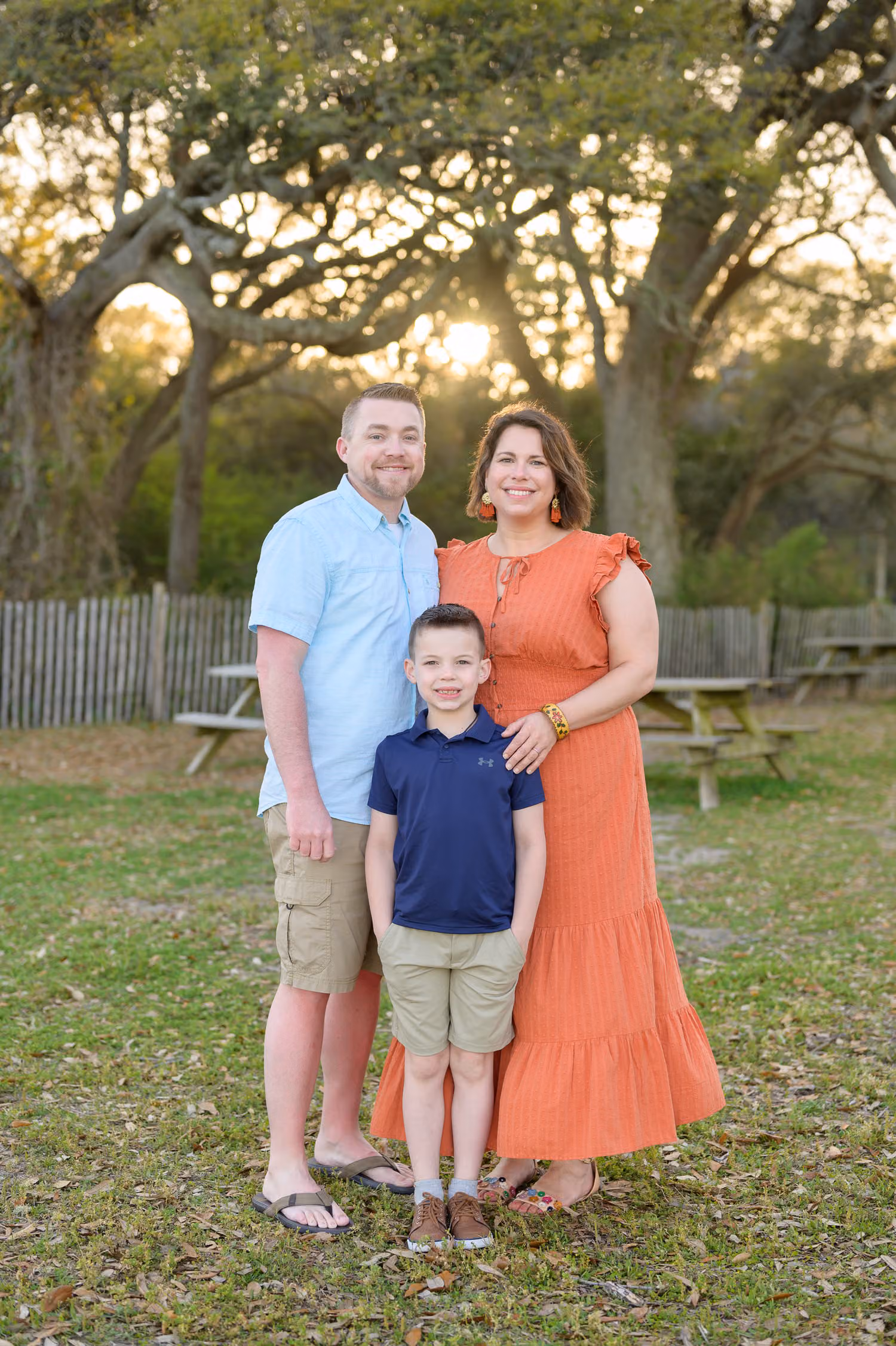 Mom, dad and son standing on the grass under twisted oaks with the sun behind them at Myrtle Beach State Park