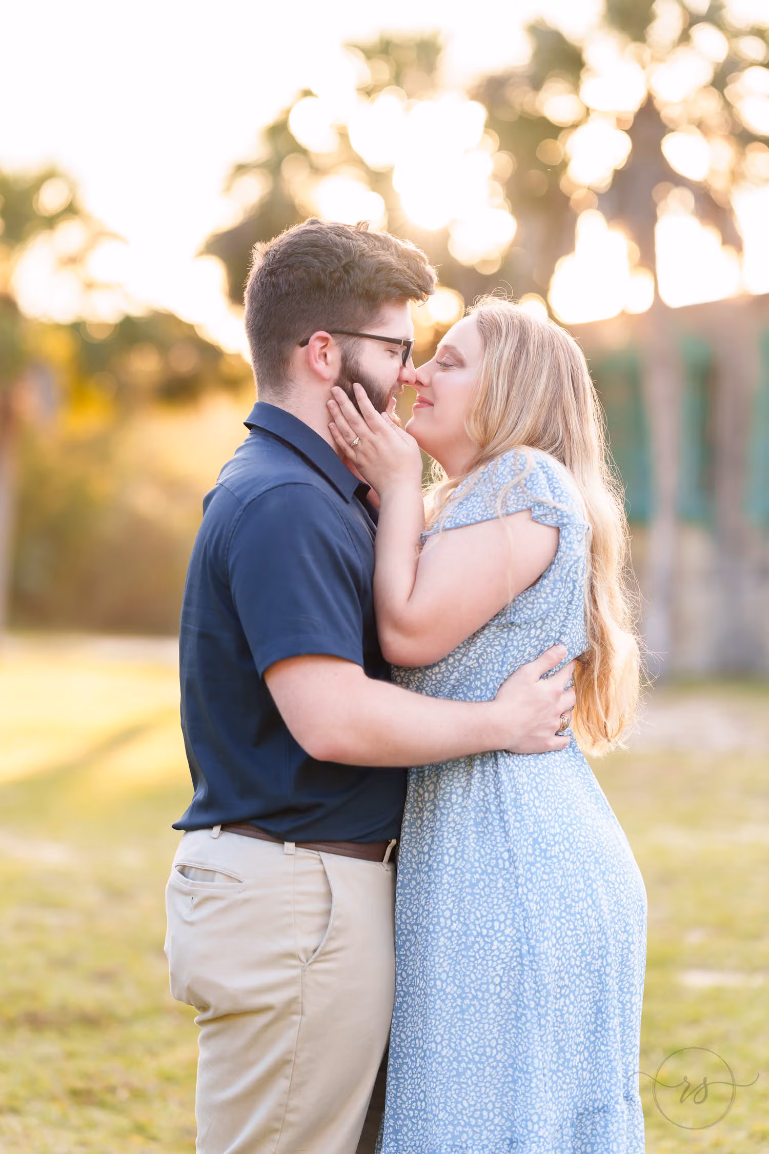 Woman kissing her fiancé's cheek as they embrace with the winter sun glowing through the palms at Huntington Beach State Park