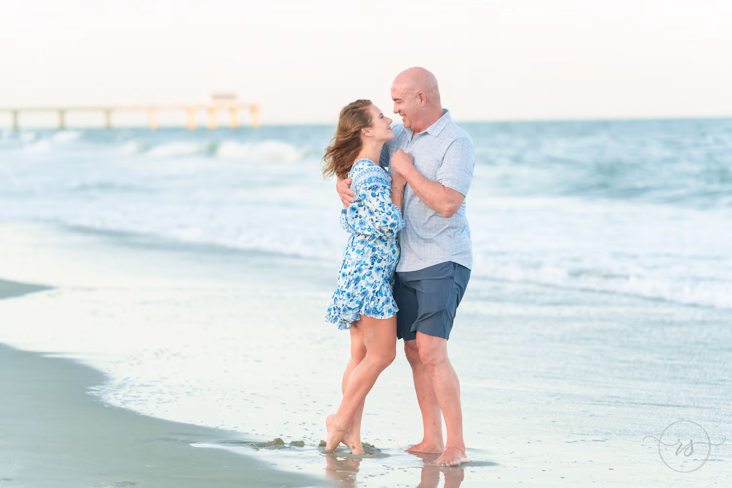 Newly engaged couple about to kiss in the shallow waves with the pier in the distance on Surfside Beach
