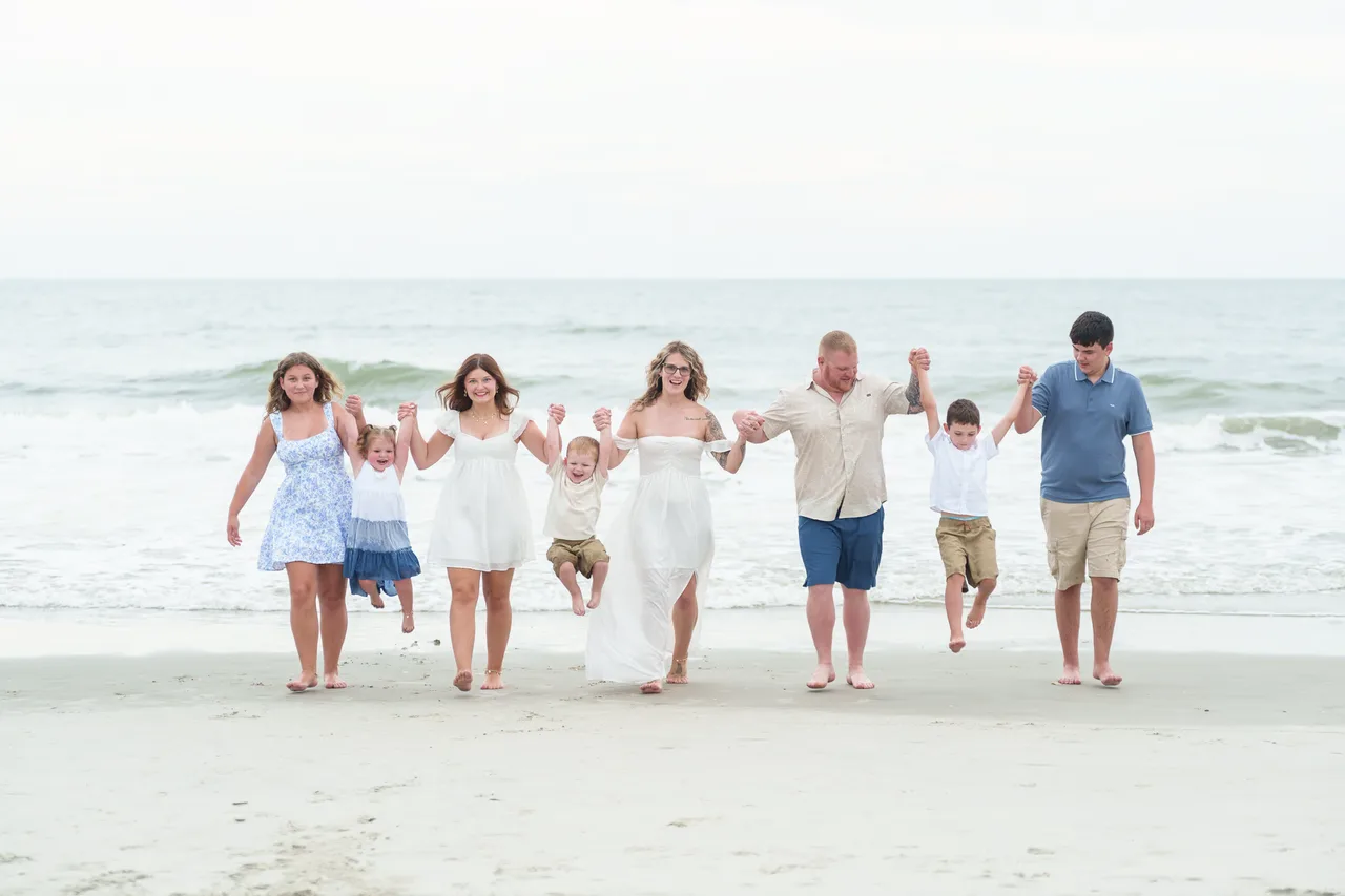 Emily's family walking hand in hand along the shore, swinging the little ones between them