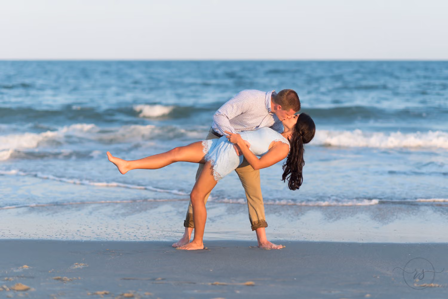 Man dipping his fiancée as she kicks up a leg in the surf at Myrtle Beach State Park
