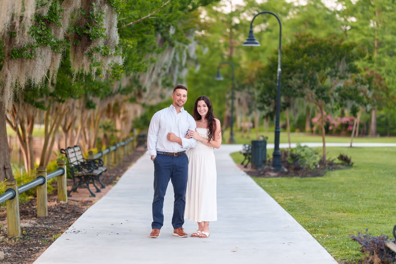 Couple standing together on a park walkway under trees hung with Spanish moss at the Conway Riverwalk