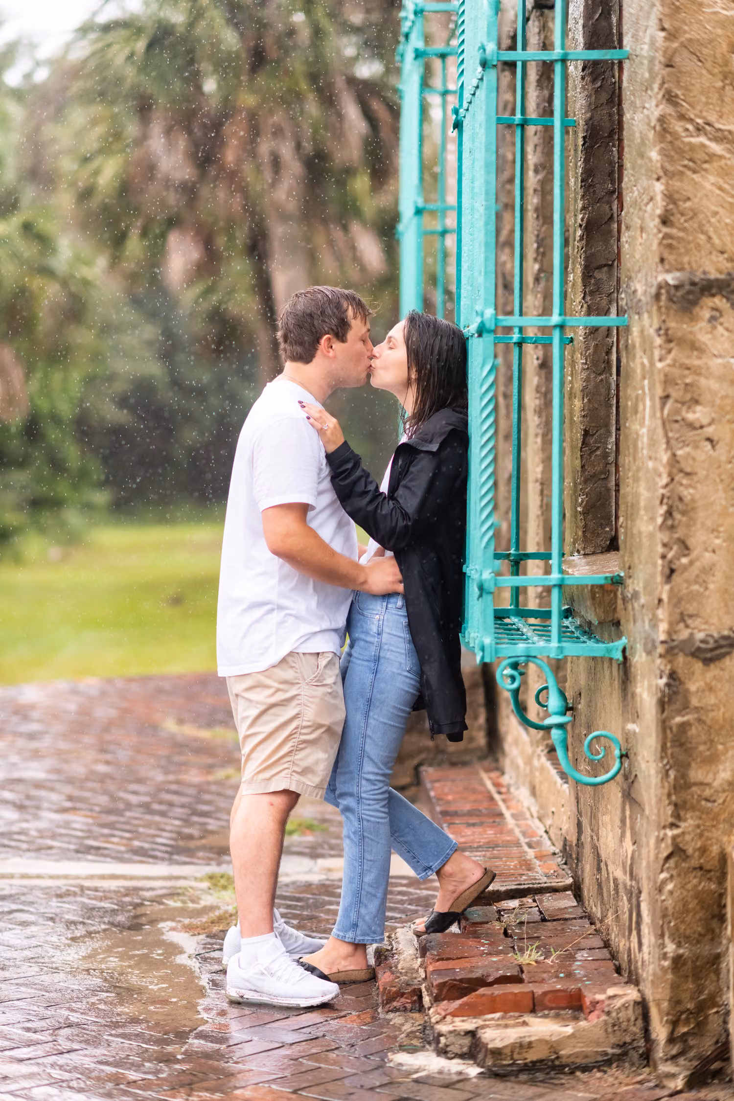 Couple kissing on wet bricks by the teal window grate of the Atalaya Castle in the rain at Huntington Beach State Park