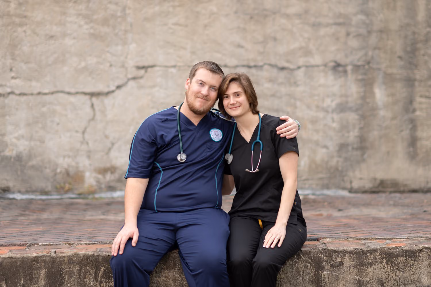 Couple in nursing scrubs with a stethoscope sitting together on a stone ledge at Huntington Beach State Park