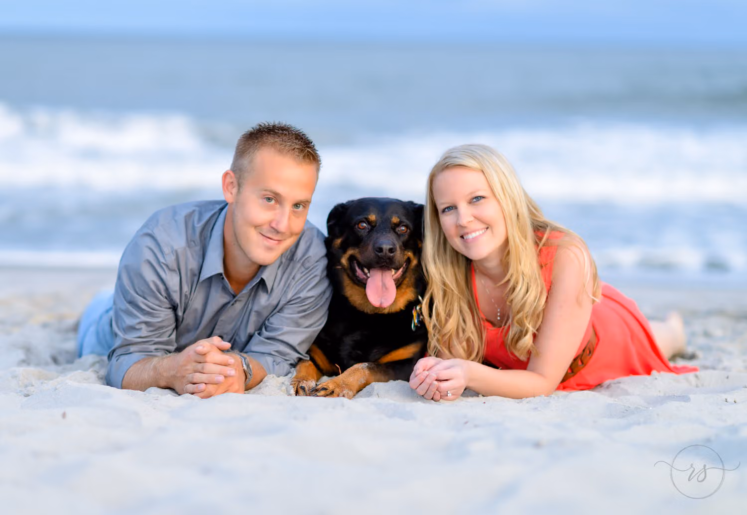 Couple lying in the sand with their black dog between them, waves breaking behind at Myrtle Beach State Park