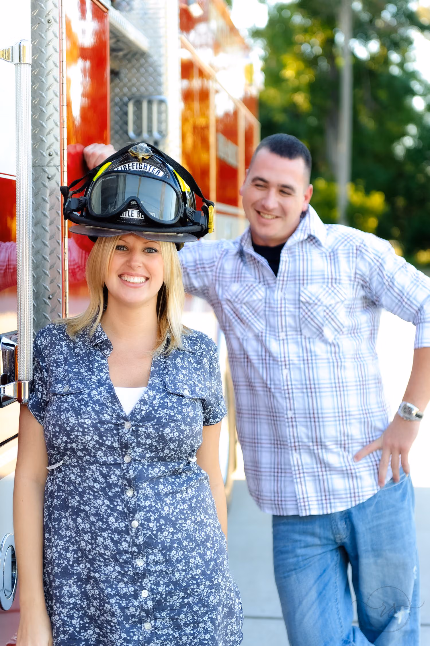 Smiling woman wearing a firefighter's helmet beside her fiancé in front of a red fire truck at Myrtle Beach Fire Station