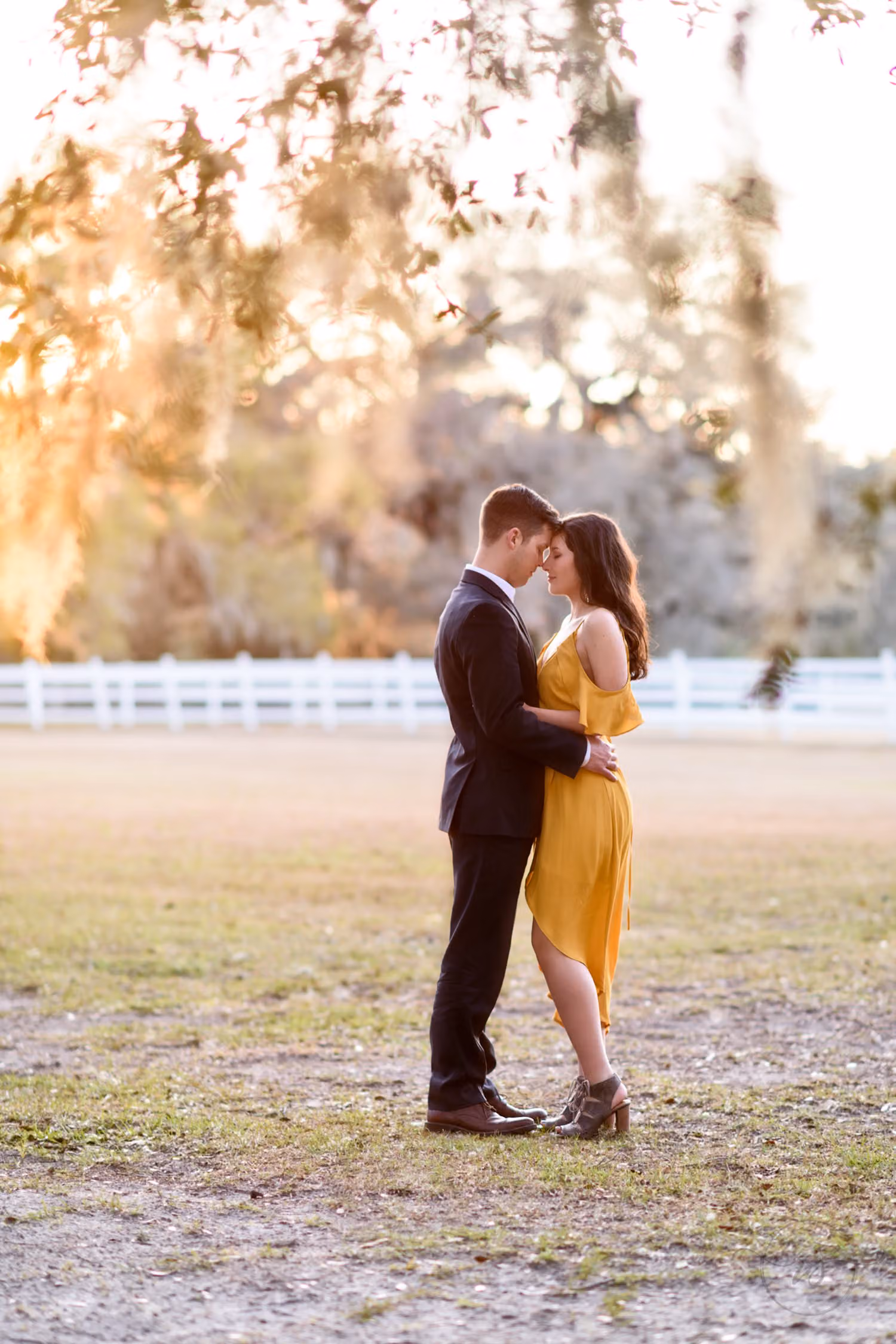 Couple in a navy suit and yellow dress touching foreheads under Spanish moss at Mansfield Plantation