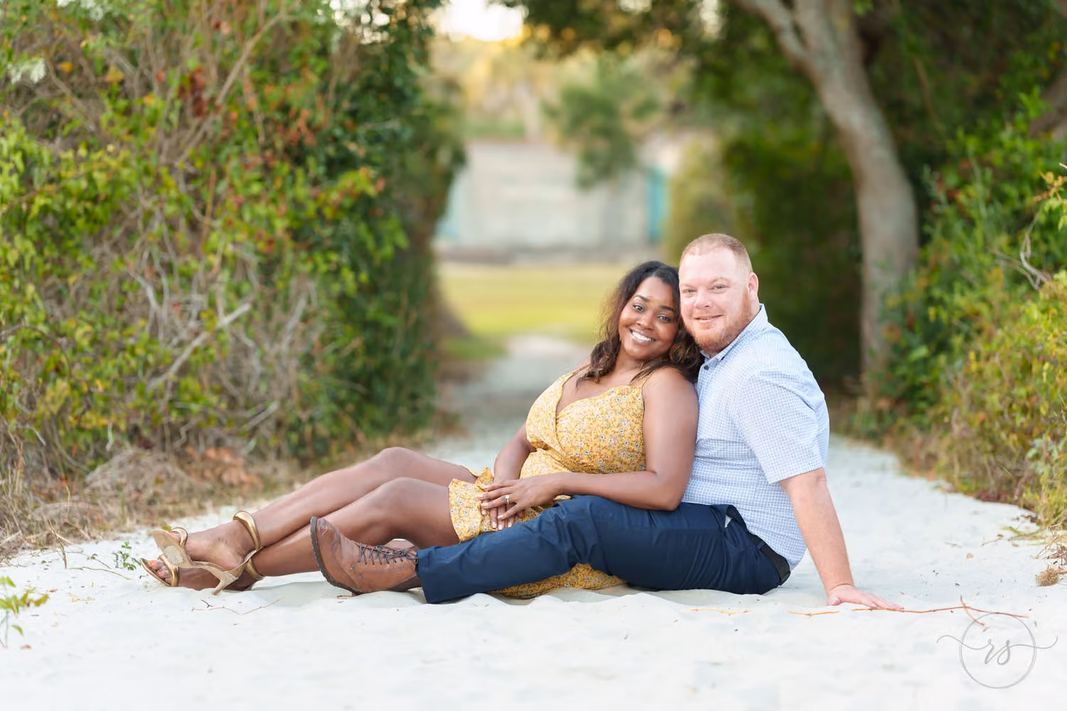 Couple sitting close together in the sand on a sheltered path to the beach at Huntington Beach State Park