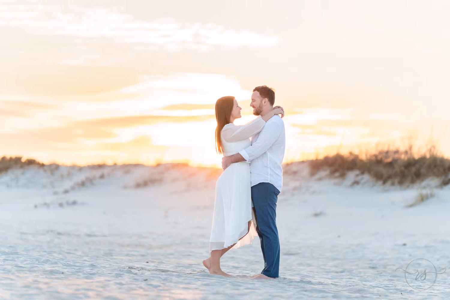 Couple embracing on the beach in front of the dunes with a soft sunset sky at Huntington Beach State Park