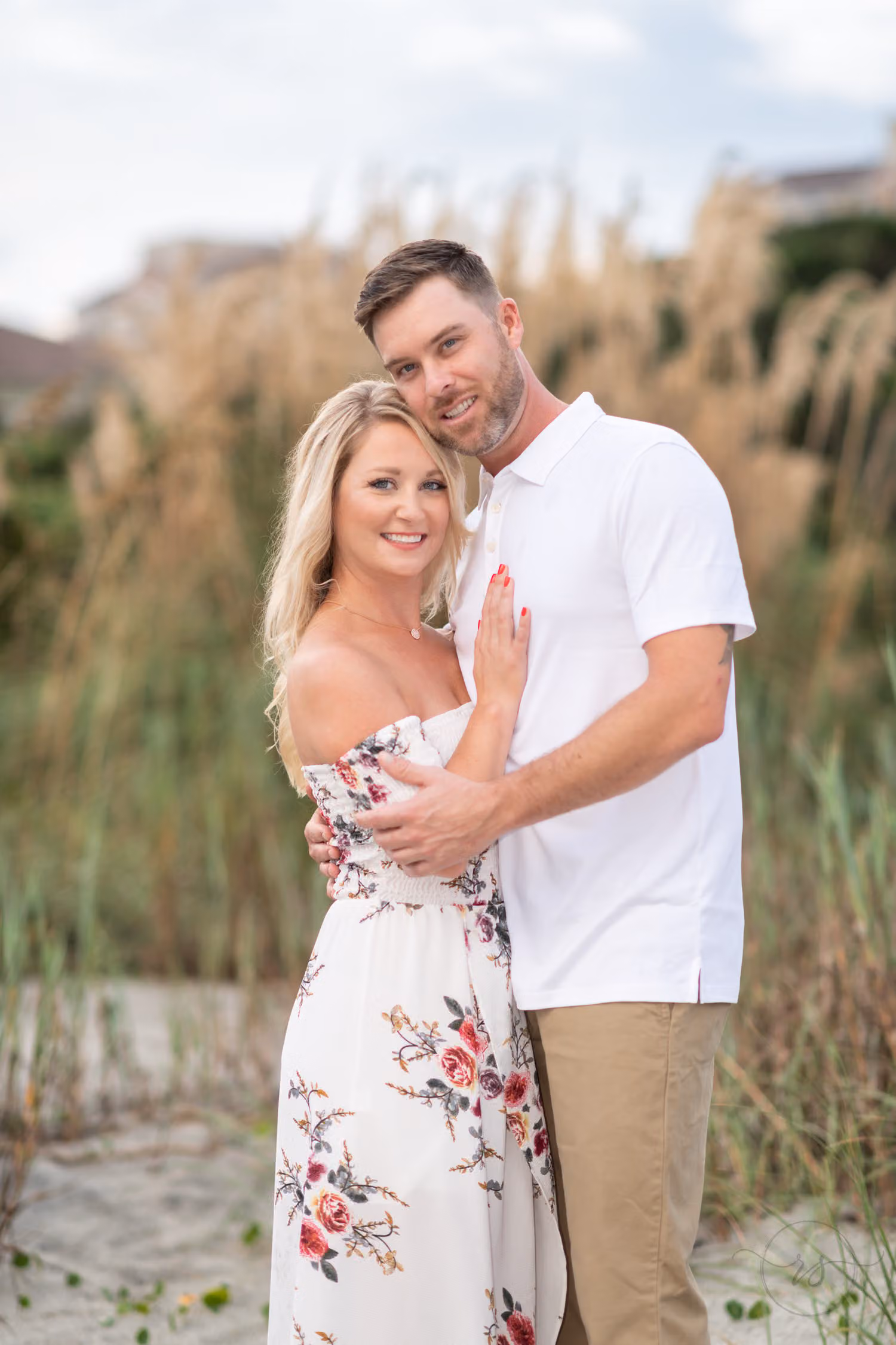 Couple hugging and smiling in front of tall beach grass on a gray evening at Grande Dunes Ocean Club