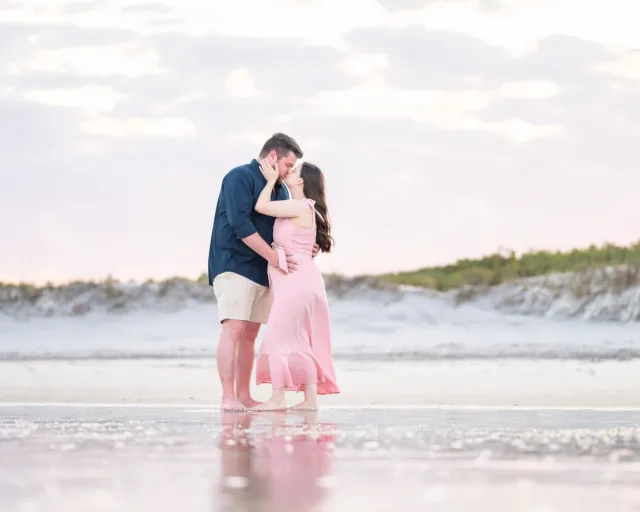 Expecting couple kissing while standing in the shallow water at the edge of the ocean at Huntington Beach State Park