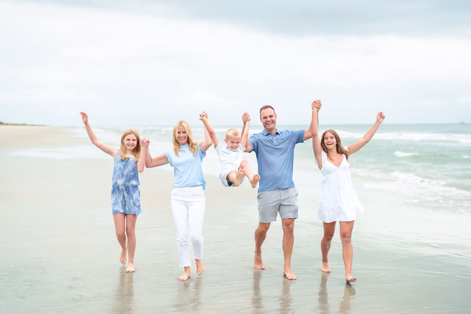 Family of five walking toward the camera with arms raised in celebration along the ocean at Huntington Beach State Park