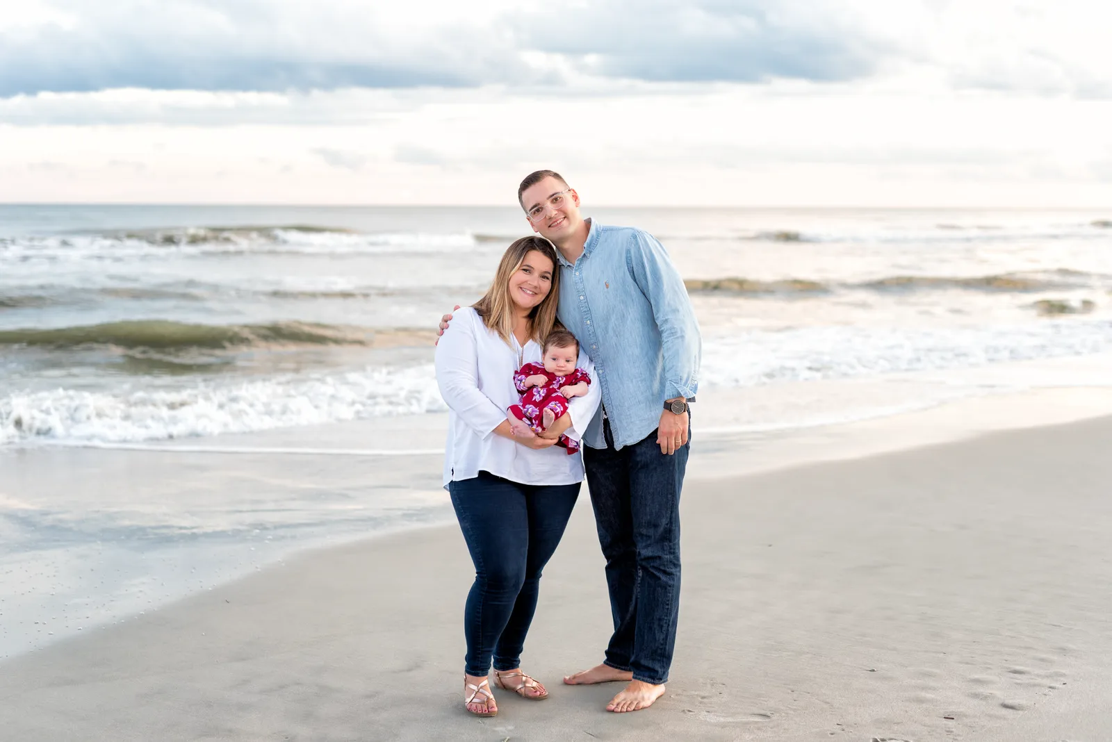 Mom and dad holding newborn by the ocean - Huntington Beach State Park