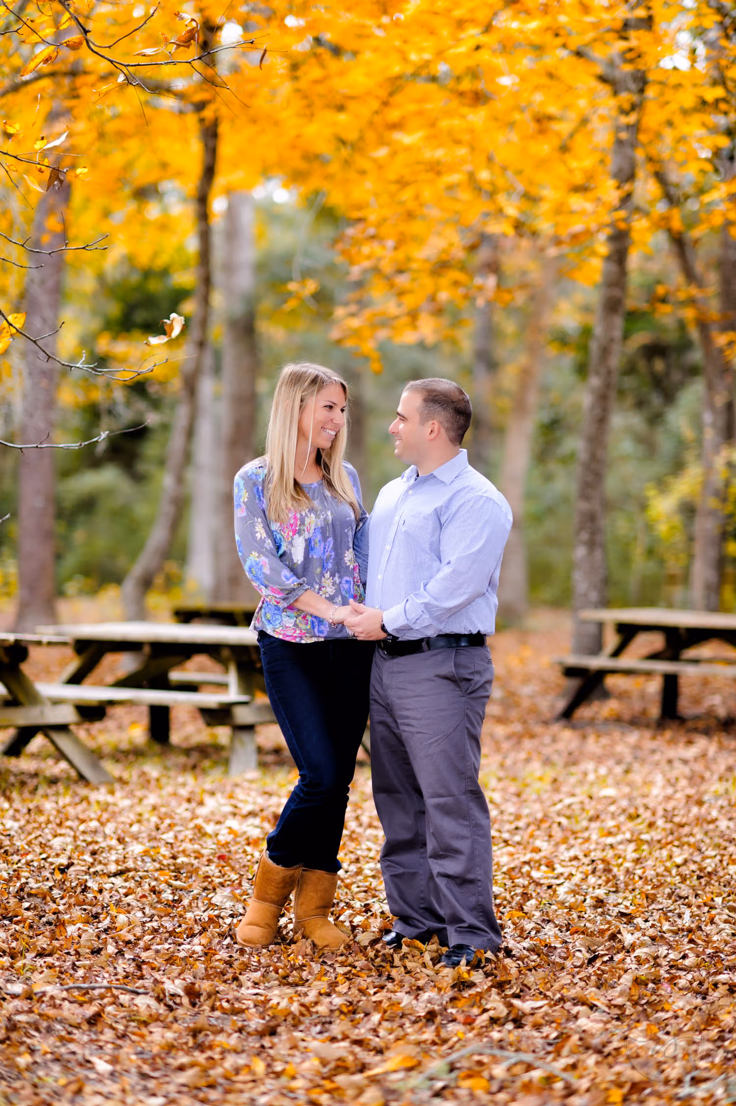 Couple standing among fallen leaves and bright yellow trees beside picnic tables at Myrtle Beach State Park