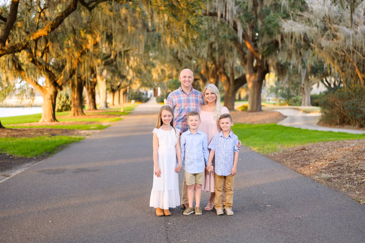 Family of five standing on the road under oaks with Spanish moss in warm golden light at Caledonia Golf & Fish Club